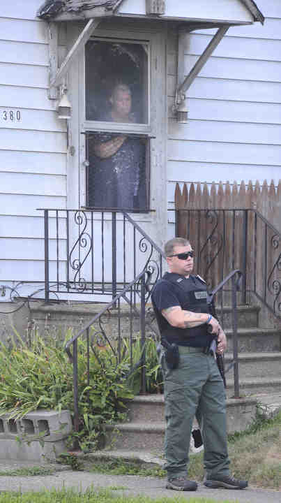 David Crow's neighbor looks out her door as an officer armed with a shotgun stands by during a standoff.   (Patricia Schaeffer / The (Lisbon) Morning Journal)